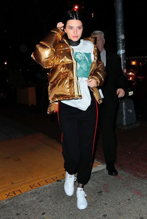 Как Kendall Jenner носит Золотая куртка-пуховик, Черная кружевная водолазка,Белая футболка с круглым вырезом с принтом, Черные спортивные штаны