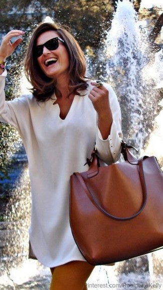 С чем носить темно-коричневую кожаную большую сумку: Дуэт бежевого свободного платья и темно-коричневой кожаной большой сумки - самый простой из возможных образов для активного выходного дня.