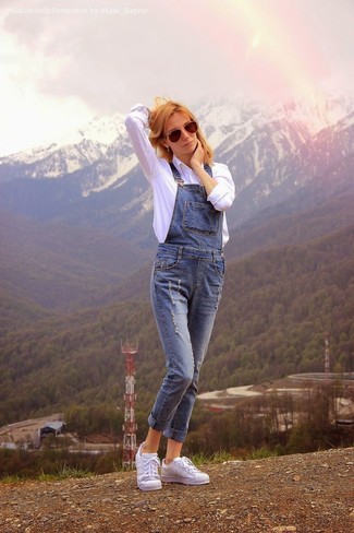 С чем носить синие джинсовые комбинезон в 30 лет: Сочетание белой классической рубашки и синих джинсовых комбинезона позволит выглядеть по моде, но при этом выразить твой индивидуальный стиль. Чтобы образ не получился слишком зализанным, можешь закончить его белыми кожаными низкими кедами.