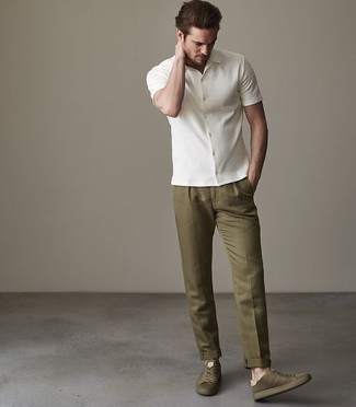 С чем носить темно-зеленые кеды мужчине: Как видишь, белая рубашка с коротким рукавом выглядит великолепно в сочетании с оливковыми брюками чинос. Такой лук легко адаптировать к повседневным реалиям, если дополнить его темно-зелеными кедами.