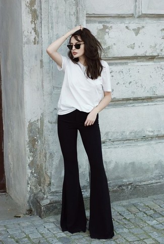 С чем носить черные джинсы-клеш в жару: Комбо из белой футболки с круглым вырезом и черных джинсов-клеш — отличный вариант для воплощения лука в стиле элегантной повседневности.