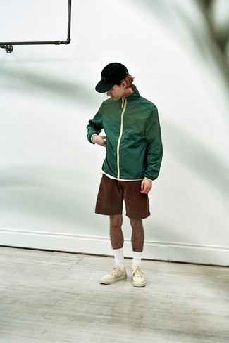 С чем носить темно-зеленую ветровку в 20 лет мужчине: Тандем темно-зеленой ветровки и коричневых шорт вдохновляет на проявление собственной индивидуальности. Что до обуви, белые низкие кеды из плотной ткани — самый подходящий вариант.