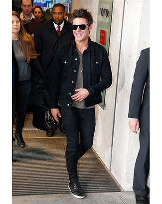Как Zac Efron носит Черная джинсовая куртка, Серая футболка с круглым вырезом с принтом, Черные зауженные джинсы, Черные низкие кеды