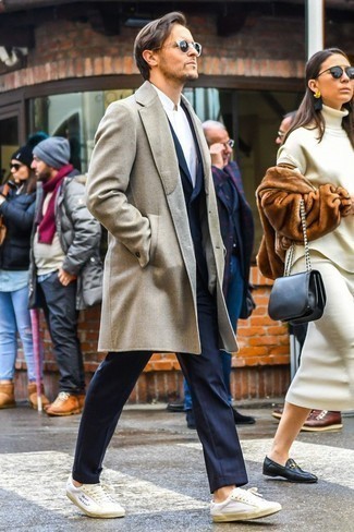 Как носить светло-коричневое длинное пальто с бело-темно-синими кожаными низкими кедами в холод: Светло-коричневое длинное пальто в сочетании с темно-синим костюмом в вертикальную полоску — замечательный пример строгого мужского стиля. Заверши лук бело-темно-синими кожаными низкими кедами, если не хочешь, чтобы он получился слишком строгим.