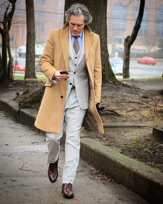 С чем носить длинное пальто за 50 лет в холод: Длинное пальто выглядит отлично в паре с серым костюмом-тройкой. Почему бы не привнести в этот лук толику легкой небрежности с помощью темно-коричневых кожаных туфель дерби?