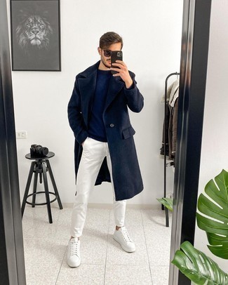 Как носить белые брюки чинос с темно-синим длинным пальто в теплую погоду в стиле смарт-кэжуал: Темно-синее длинное пальто и белые брюки чинос прекрасно впишутся в любой мужской образ — лёгкий повседневный образ или же строгий вечерний. Ты можешь легко адаптировать такой образ к повседневным нуждам, надев белыми кожаными низкими кедами.