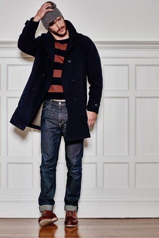 Модный лук: темно-синее длинное пальто, коричневый свитер с круглым вырезом в горизонтальную полоску, темно-синие джинсы, темно-красные кожаные рабочие ботинки