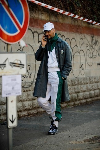 Модный лук: черное кожаное длинное пальто, бело-зеленый спортивный костюм, черно-белые кроссовки, белая бейсболка