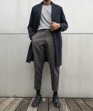 Как носить серые брюки чинос с черными кожаными туфлями дерби в 30 лет в прохладную погоду: Если ты принадлежишь к той когорте мужчин, которые любят выглядеть стильно, тебе полюбится образ из темно-синего длинного пальто и серых брюк чинос. Любители экспериментов могут дополнить образ черными кожаными туфлями дерби, тем самым добавив в него немного строгости.