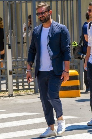 Модный лук: темно-синий костюм, белая футболка с круглым вырезом, белые кожаные низкие кеды, серые солнцезащитные очки