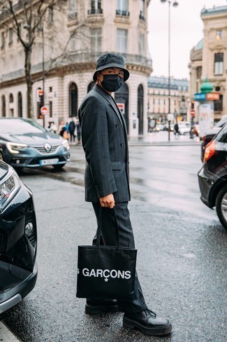 Модный мужской лук: темно-синий костюм в вертикальную полоску, темно-синяя футболка с круглым вырезом, черные кожаные массивные туфли дерби, черно-белая большая сумка из плотной ткани с принтом