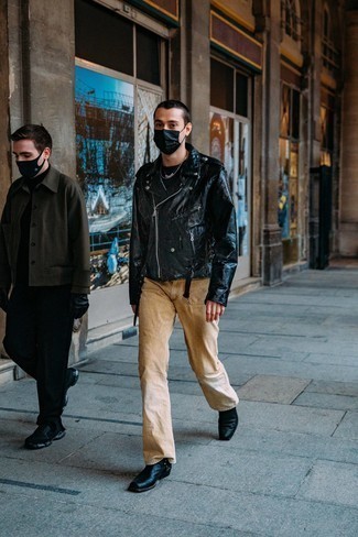 Модный мужской лук: черная кожаная косуха, черная футболка с круглым вырезом, светло-коричневые джинсы, черные кожаные ботинки челси