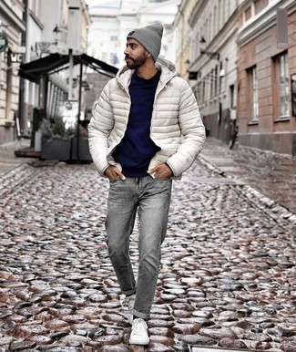 С чем носить темно-серые джинсы мужчине в прохладную погоду: Сочетание белой куртки-пуховика и темно-серых джинсов подойдет и для работы в офисе, и для вечера с друзьями. Ты сможешь легко приспособить такой образ к повседневным реалиям, закончив его белыми низкими кедами из плотной ткани.