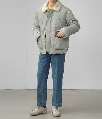 Модный лук: серая куртка-пуховик, горчичная футболка с круглым вырезом, синие джинсы, белые низкие кеды из плотной ткани