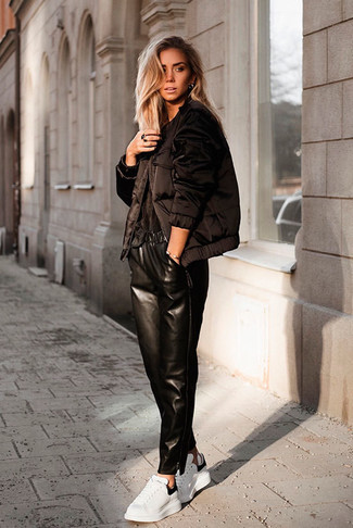 Модный лук: черная куртка-пуховик, черная футболка с круглым вырезом, черные кожаные пижамные штаны, белые кожаные низкие кеды
