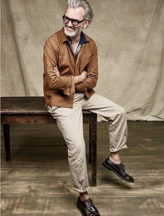 С чем носить темно-синюю джинсовую рубашку за 50 лет мужчине в стиле смарт-кэжуал: Темно-синяя джинсовая рубашка и светло-коричневые брюки чинос — необходимые элементы в гардеробе любителей стиля casual. Теперь почему бы не привнести в повседневный лук немного изысканности с помощью темно-коричневых кожаных брогов?