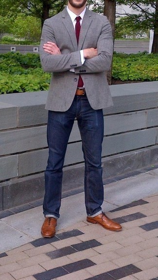 Как носить темно-синие джинсы с коричневыми кожаными оксфордами в 30 лет: Серый пиджак и темно-синие джинсы выигрышно вписываются в гардероб самых взыскательных мужчин. Любители экспериментов могут завершить ансамбль коричневыми кожаными оксфордами, тем самым добавив в него немного строгости.