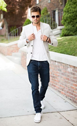Как носить белые плимсоллы с бежевым пиджаком мужчине: Бежевый пиджак в сочетании с темно-синими джинсами — превосходный пример вольного офисного стиля для парней. Пара белых плимсоллов добавит облику легкости и беззаботства.