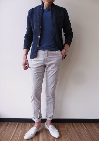 С чем носить темно-синий вязаный пиджак мужчине лето в стиле смарт-кэжуал: Темно-синий вязаный пиджак в сочетании с бежевыми брюками чинос в вертикальную полоску продолжает импонировать джентльменам, которые всегда одеты со вкусом. И почему бы не привнести в повседневный образ немного изысканности с помощью белых замшевых лоферов? Подобное сочетание вещей даст тебе ощущение комфорта в зной и уверенность в том, что ты выглядишь на все сто.