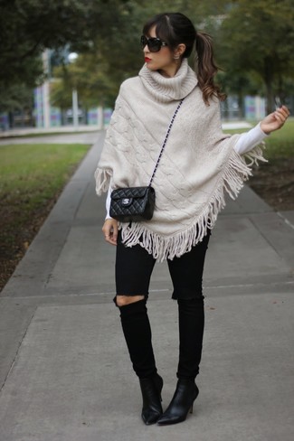 Модный лук: бежевое вязаное пончо, белый свитер с круглым вырезом, черные рваные джинсы скинни, черные замшевые ботильоны