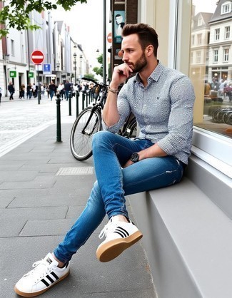 Модный мужской лук: бело-темно-синяя рубашка с длинным рукавом в мелкую клетку, синие джинсы, бело-черные кожаные низкие кеды, черные кожаные часы