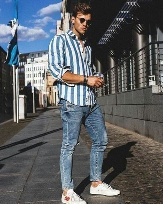 Как носить синие джинсы с белыми низкими кедами из плотной ткани мужчине в теплую погоду: Если ты ценишь комфорт и практичность, бело-синяя рубашка с длинным рукавом в вертикальную полоску и синие джинсы — хороший вариант для стильного повседневного мужского образа. Очень выигрышно здесь выглядят белые низкие кеды из плотной ткани.