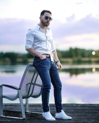 Как носить темно-синие джинсы с белыми низкими кедами из плотной ткани мужчине лето: Белая рубашка с длинным рукавом и темно-синие джинсы — идеальный вариант, если ты ищешь расслабленный, но в то же время стильный мужской образ. Белые низкие кеды из плотной ткани — прекрасный выбор, чтобы завершить ансамбль. Подобный образ непременно придется тебе по вкусу в жаркую погоду.