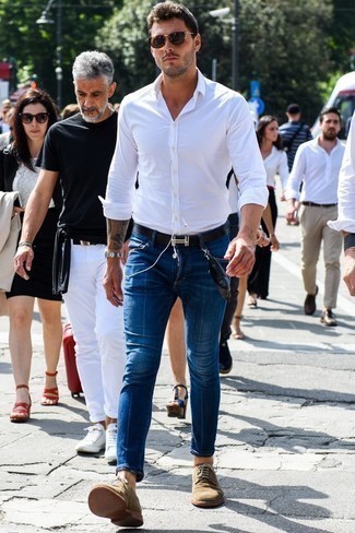 С чем носить синие зауженные джинсы мужчине лето в стиле смарт-кэжуал: Дуэт белой рубашки с длинным рукавом и синих зауженных джинсов позволит реализовать в твоем образе городской стиль современного молодого человека. Преобразить ансамбль и добавить в него толику классики позволят светло-коричневые замшевые туфли дерби. Такой лук определенно поможет пережить изнурительную летнюю жару.