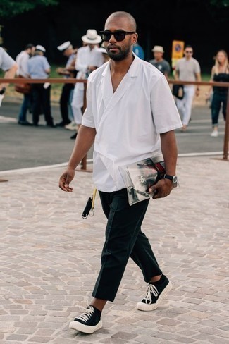 Модный лук: белая рубашка с коротким рукавом, темно-синие брюки чинос, черно-белые низкие кеды из плотной ткани, черные солнцезащитные очки
