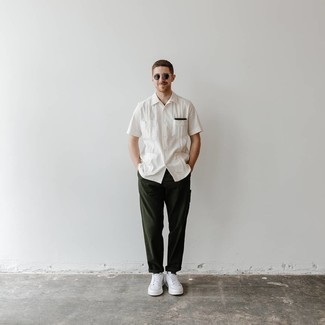 Модный лук: белая рубашка с коротким рукавом, темно-зеленые брюки чинос, белые кожаные низкие кеды, темно-зеленые солнцезащитные очки