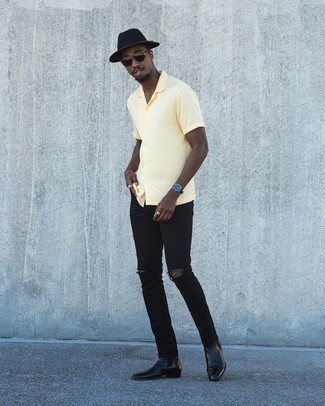 Модный лук: желтая рубашка с коротким рукавом, черные рваные зауженные джинсы, черные кожаные ботинки челси, черная шерстяная шляпа