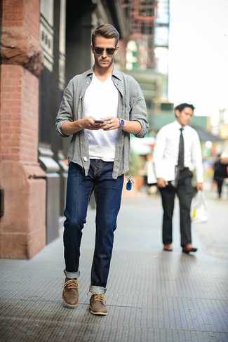 Модный лук: серая рубашка с длинным рукавом, белая футболка с v-образным вырезом, темно-синие джинсы, темно-коричневые кожаные ботинки дезерты