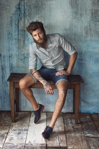 С чем носить темно-синие джинсовые шорты мужчине лето: Комбо из серой рубашки с длинным рукавом из шамбре и темно-синих джинсовых шорт не прекращает импонировать молодым людям, которые всегда одеты с иголочки. Темно-синие замшевые туфли дерби добавят образу нотки классики. Подобное сочетание даст комфорт и удобство в зной.