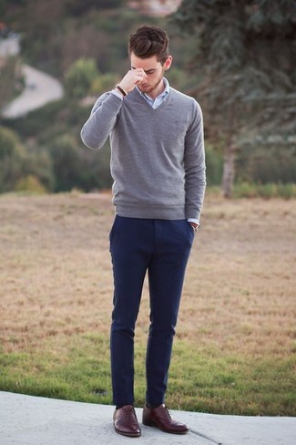 Модный лук: серый свитер с v-образным вырезом, белая рубашка с длинным рукавом, темно-синие брюки чинос, коричневые кожаные оксфорды