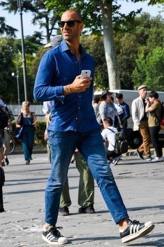 Как носить темно-синюю рубашку с длинным рукавом с синими джинсами мужчине: Если у тебя на работе нет дресс-кода как такового, обрати внимание на такое сочетание темно-синей рубашки с длинным рукавом и синих джинсов. Пара черно-белых кожаных низких кед позволит сделать образ более целостным.