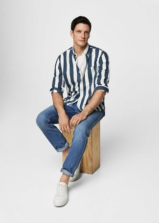 Модный лук: темно-сине-белая рубашка с длинным рукавом в вертикальную полоску, белая футболка с круглым вырезом, синие джинсы, белые кожаные низкие кеды