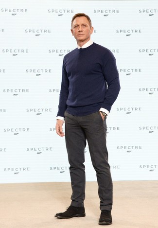 Как Daniel Craig носит Темно-синий свитер с круглым вырезом, Белая классическая рубашка, Темно-коричневые шерстяные классические брюки, Темно-коричневые замшевые ботинки дезерты