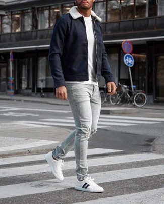 Как носить серые джинсы с белыми низкими кедами мужчине в теплую погоду в спортивном стиле: Если в одежде ты делаешь ставку на удобство и функциональность, темно-синяя куртка харрингтон и серые джинсы — замечательный выбор для расслабленного мужского образа на каждый день. Что касается обуви, белые низкие кеды — самый удачный вариант.