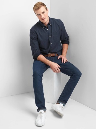 Как носить темно-синие джинсы с белыми кожаными низкими кедами мужчине в стиле кэжуал: Если ты любишь одеваться с иголочки, чувствуя себя при этом комфортно и уверенно, стоит попробовать это сочетание темно-синей рубашки с длинным рукавом в горошек и темно-синих джинсов. Белые кожаные низкие кеды — отличный выбор, чтобы завершить лук.
