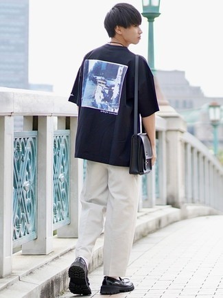 Модный мужской лук: черная футболка с круглым вырезом с принтом, белые брюки чинос, черные кожаные лоферы, черная кожаная сумка почтальона