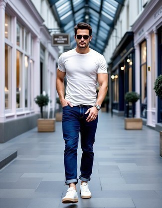 Модный мужской лук: белая футболка с круглым вырезом, темно-синие джинсы, белые низкие кеды из плотной ткани, темно-коричневые солнцезащитные очки