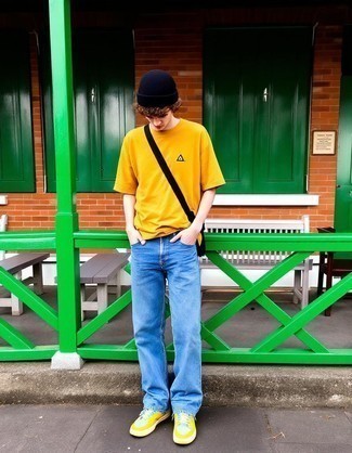 Модный мужской лук: горчичная футболка с круглым вырезом, голубые джинсы, разноцветные кожаные низкие кеды, черная сумка почтальона из плотной ткани