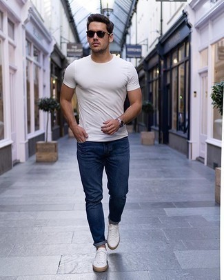 С чем носить темно-синие джинсы мужчине в жару: Белая футболка с круглым вырезом в паре с темно-синими джинсами поможет подчеркнуть твой личный стиль. Белые низкие кеды из плотной ткани станут превосходным завершением твоего образа.