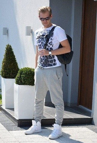 Модный мужской лук: бело-темно-синяя футболка с круглым вырезом с принтом, серые спортивные штаны, белые кожаные высокие кеды, черный рюкзак из плотной ткани