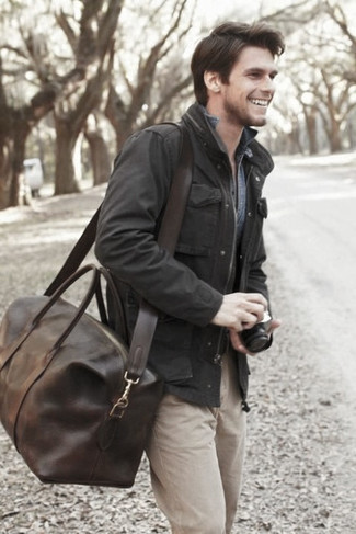 С чем носить коричневую дорожную сумку мужчине в теплую погоду в стиле кэжуал: Для выходного дня в компании друзей прекрасно подойдет сочетание черной полевой куртки и коричневой дорожной сумки.