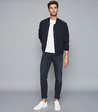 Модный лук: черная университетская куртка, белая футболка с круглым вырезом, темно-синие джинсы, белые низкие кеды из плотной ткани
